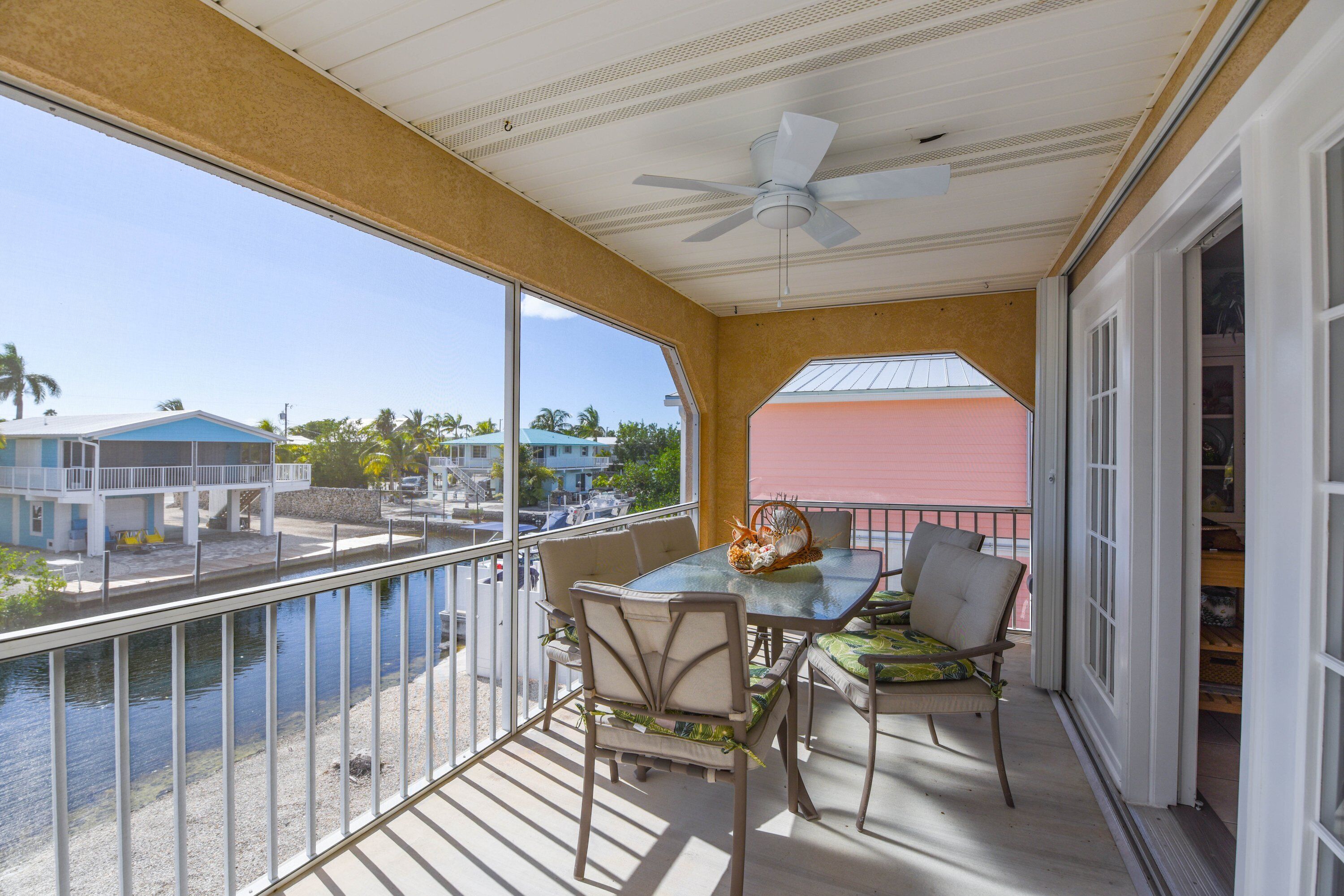 A balcony with a table and chairs, a ceiling fan, and a view of a water body and buildings.