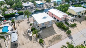 Vue aérienne d’un quartier résidentiel situé sur la côte, avec des maisons, une piscine et des bateaux.