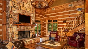 A log cabin interior with a stone fireplace, leather furniture, and a wooden staircase. - Selah Springs Ranch- Large Family Reunion/Retreat Ranch on the River- Sleeps 60 (Brady)