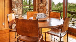 A rustic dining area with a stone wall, wooden ceiling beams, and a large window offering a view of greenery. - Selah Springs Ranch- Large Family Reunion/Retreat Ranch on the River- Sleeps 60 (Brady)