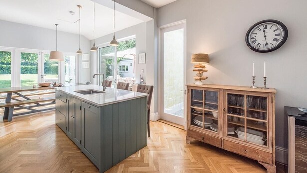 Une cuisine moderne dotée d’un îlot central, de luminaires suspendus et offrant une vue sur l’extérieur.