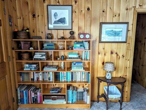 A wooden bookshelf filled with books, a framed picture, a clock, and a small table with a lamp.