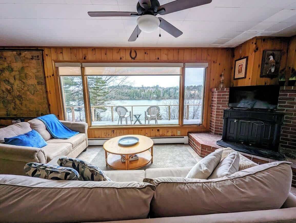 A cozy living room with a fireplace, a ceiling fan, and large windows overlooking a lake.