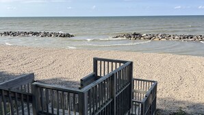 En træterrasse med gelændinger med udsigt over en sandstrand og en klippefyldt kystlinje.