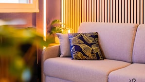 Een moderne woonkamer met een bank, een potplant en een raam met zonwering.