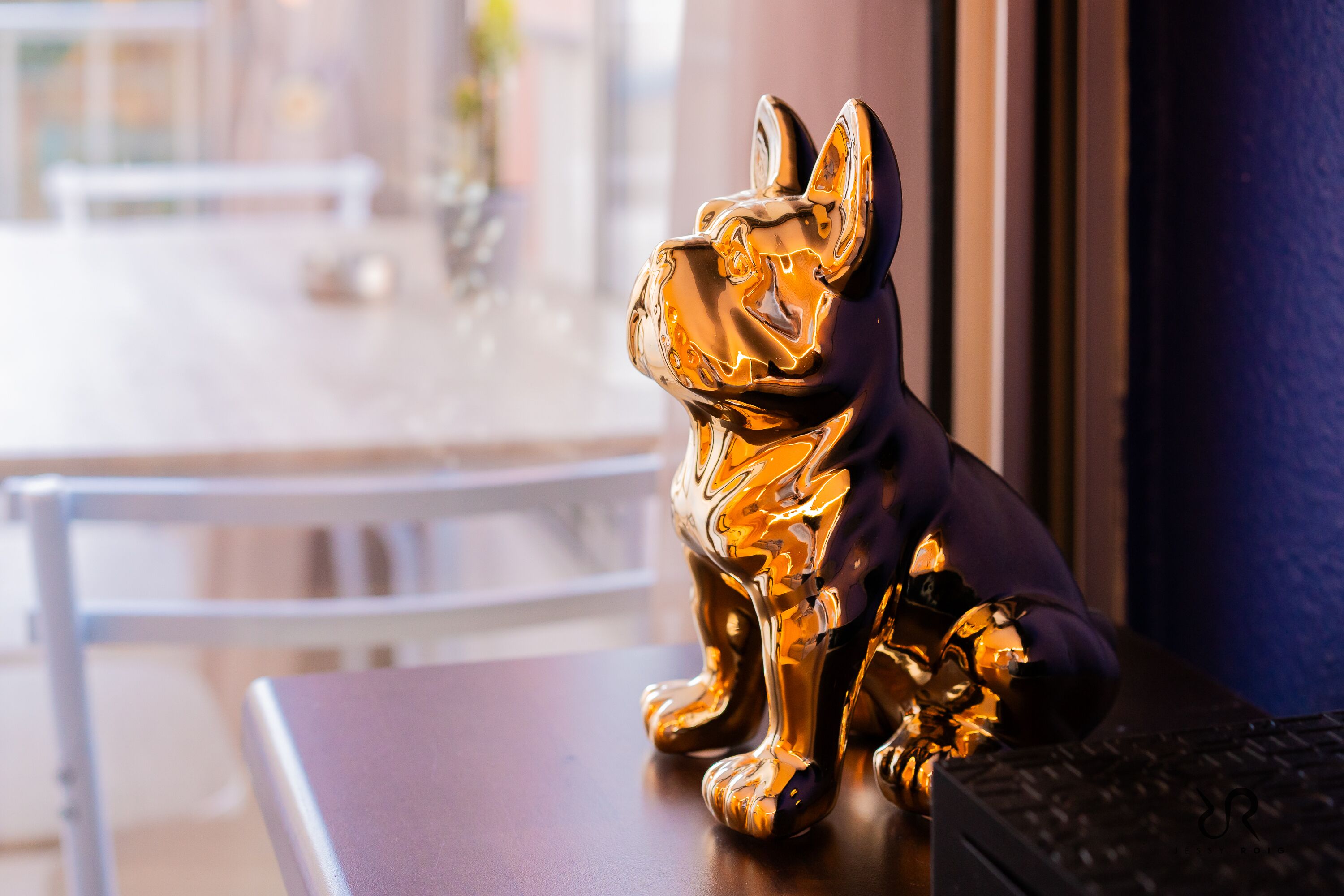 Une statuette de chien dorée, posée sur une table en bois près d’une fenêtre.