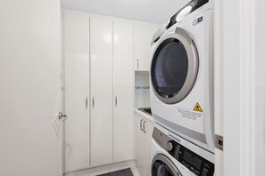 A laundry room with a stacked washer and dryer, a white wardrobe, and a tiled floor.