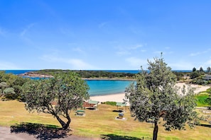 Een kustlandschap met een strand, picknickplaatsen en bomen.