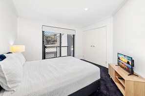 A bedroom with a bed, a TV on a wooden stand, a door, and a window with a view. - Ocean Views Beachfront Escape at Boat Harbour (Boat Harbour)