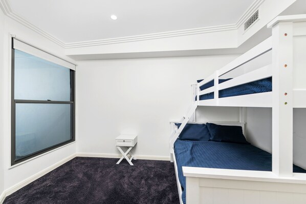 A room with bunk beds, a small bedside table, and a window.