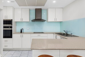 A modern kitchen with white cabinets, a stainless steel range hood, a built-in oven, and a sink with a faucet.