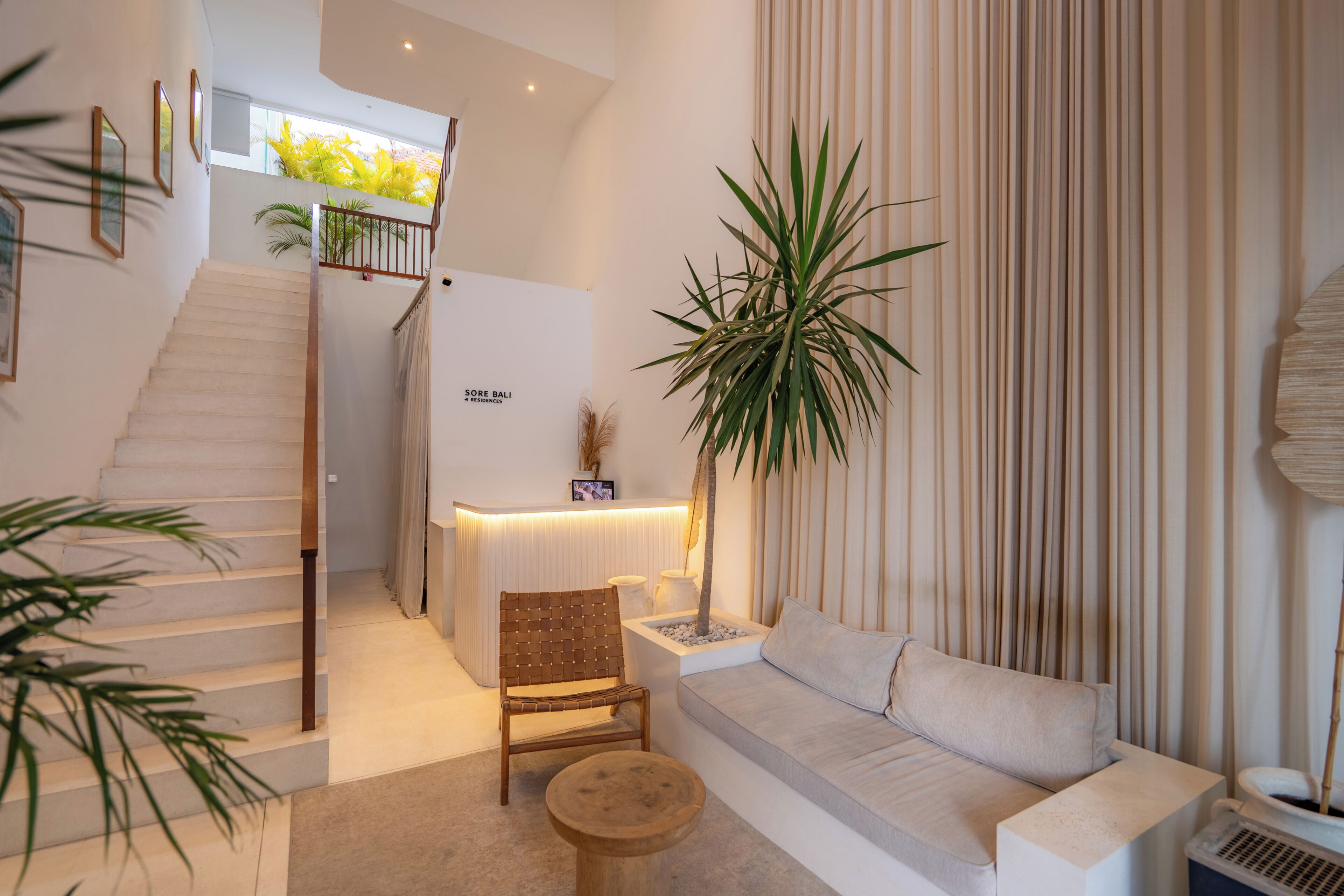 A modern interior with a staircase, a reception desk, a sofa, and a large plant.