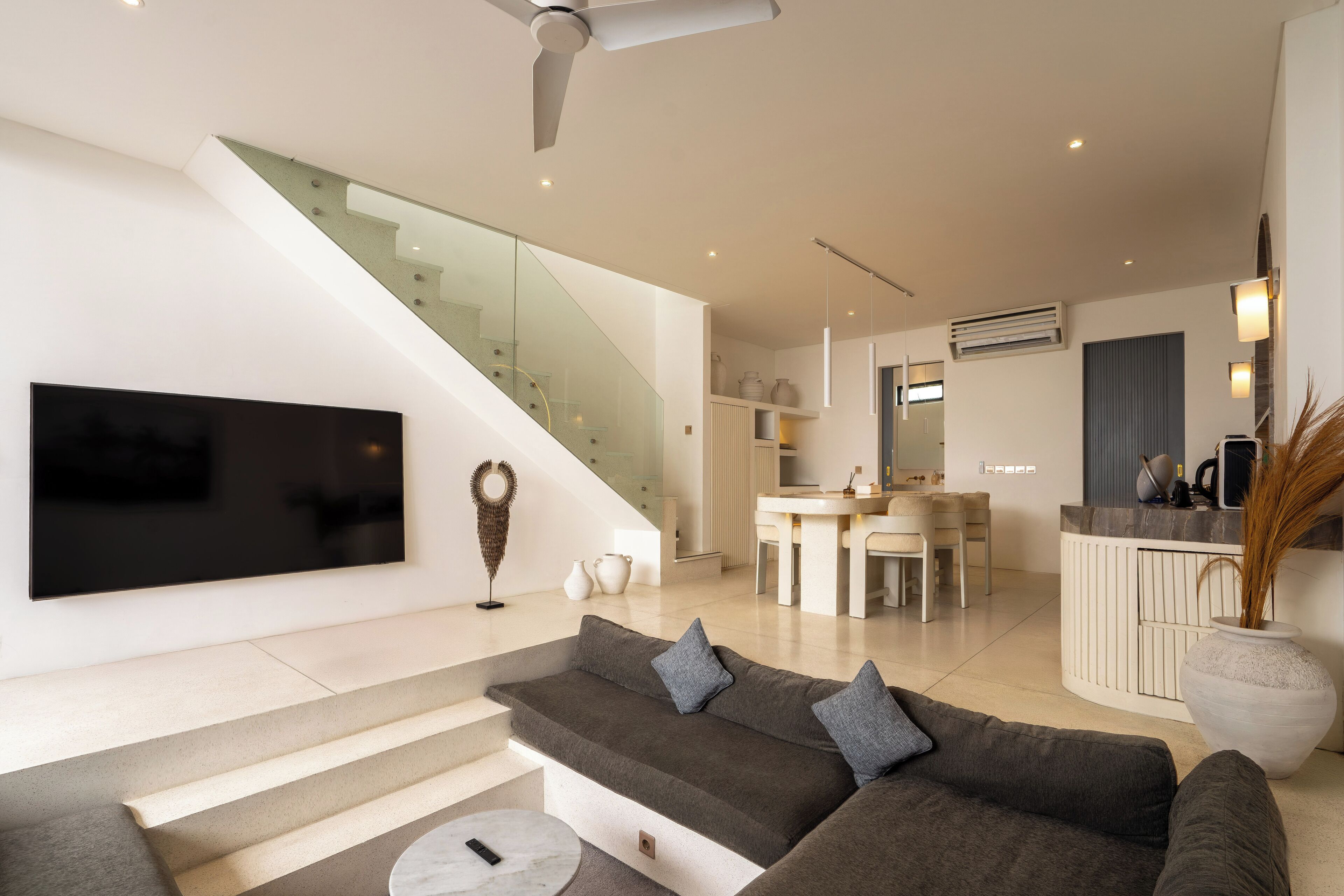 Una sala de estar moderna con un televisor de pantalla plana grande, un sofá seccional gris, una escalera y una zona de cocina.