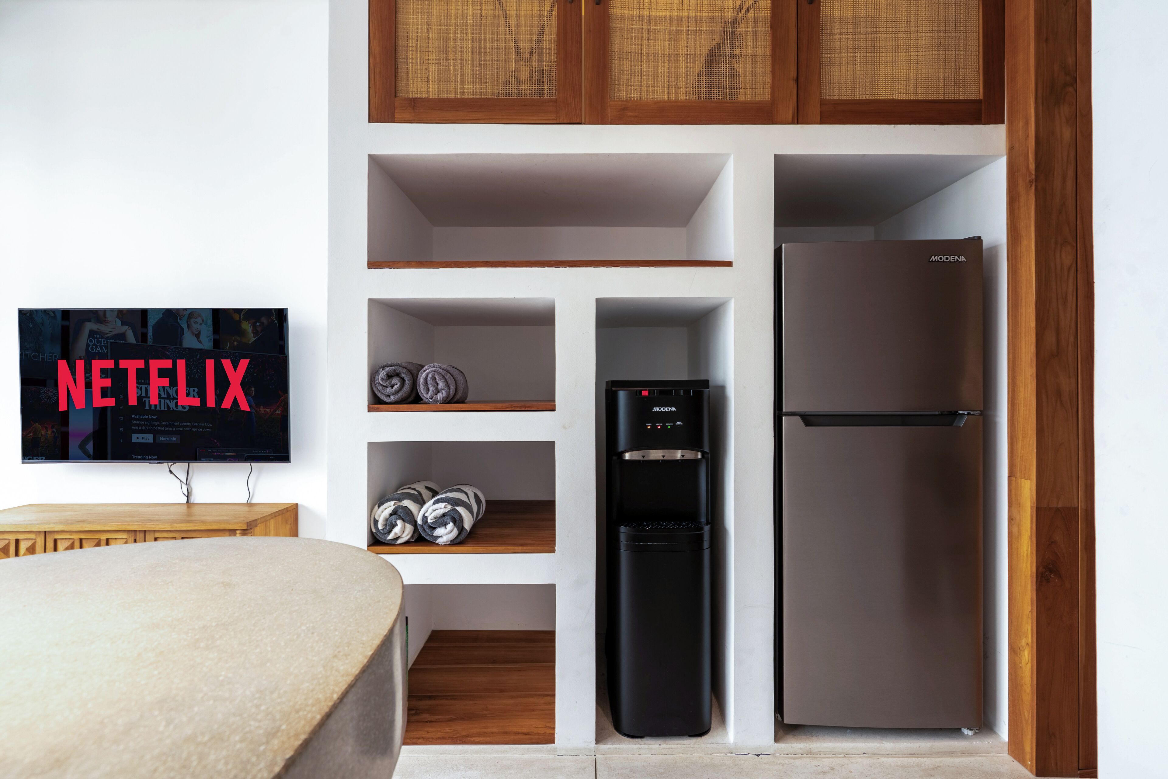 A modern kitchen with a built-in refrigerator, a water dispenser, and a flat-screen TV mounted on the wall.