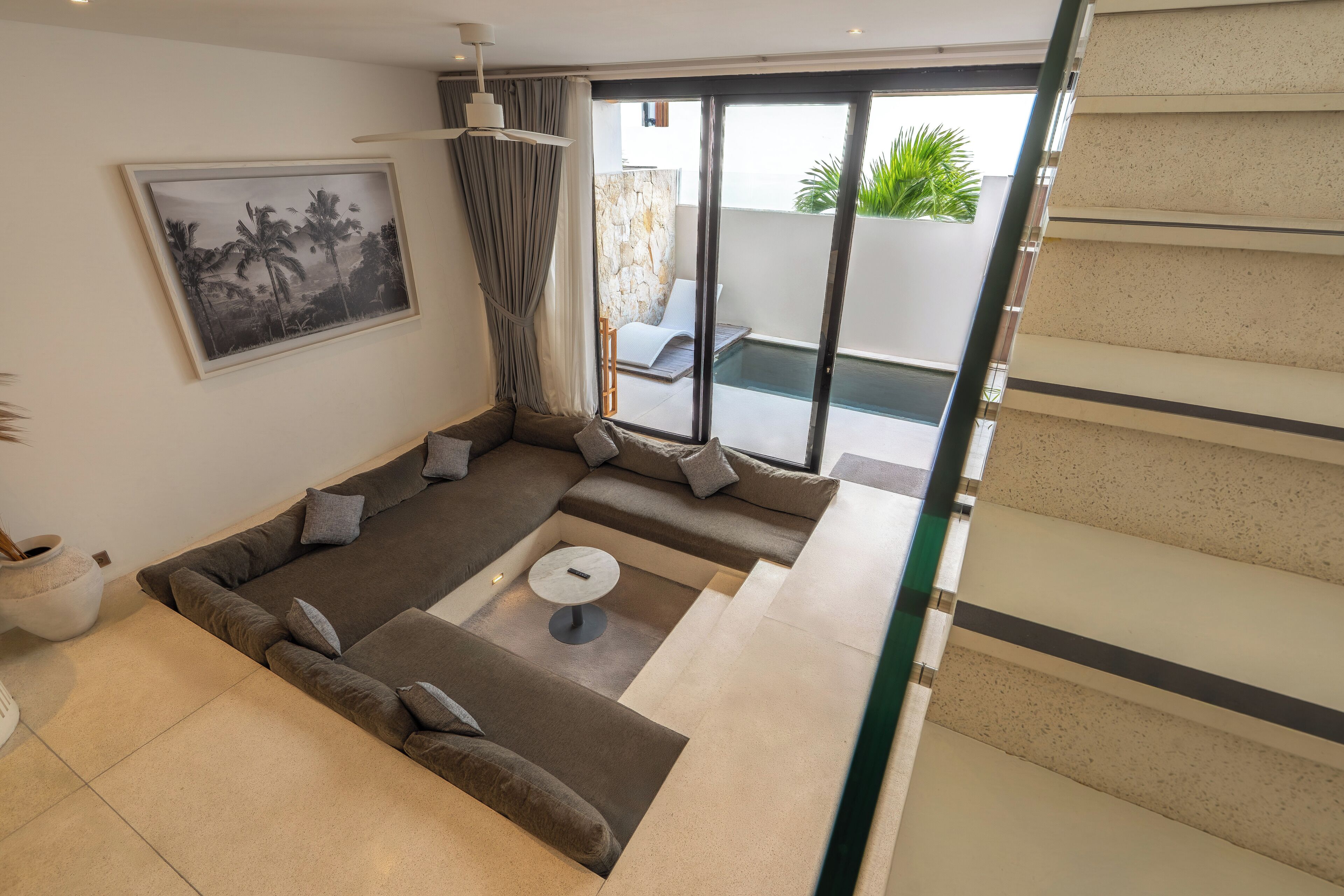 Una sala de estar moderna con un sofá modular, una mesa de centro y un amplio ventanal con vista a una piscina y follaje.