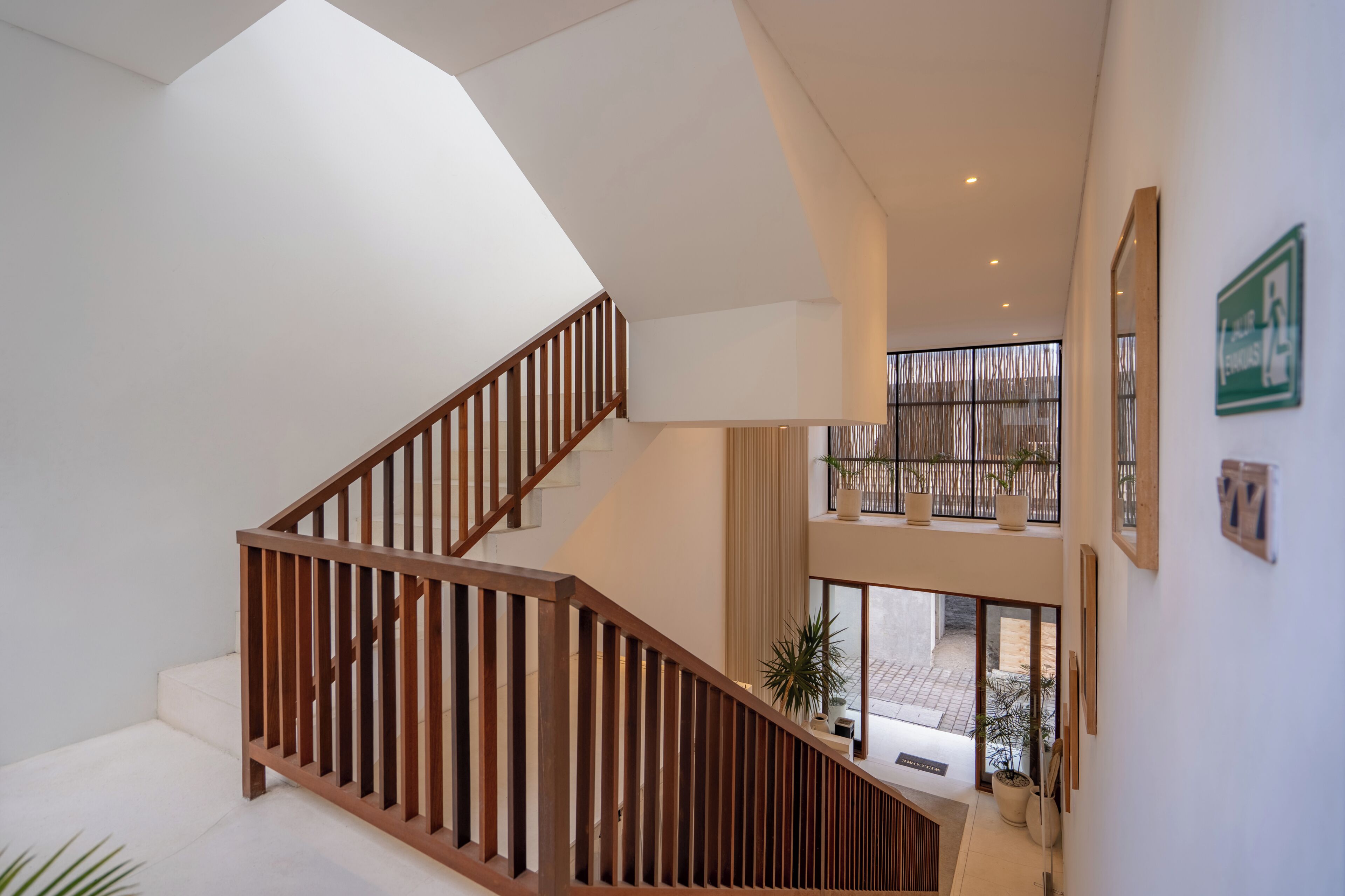 Un interior moderno con una escalera de madera, un balcón en el segundo piso y vistas al exterior.