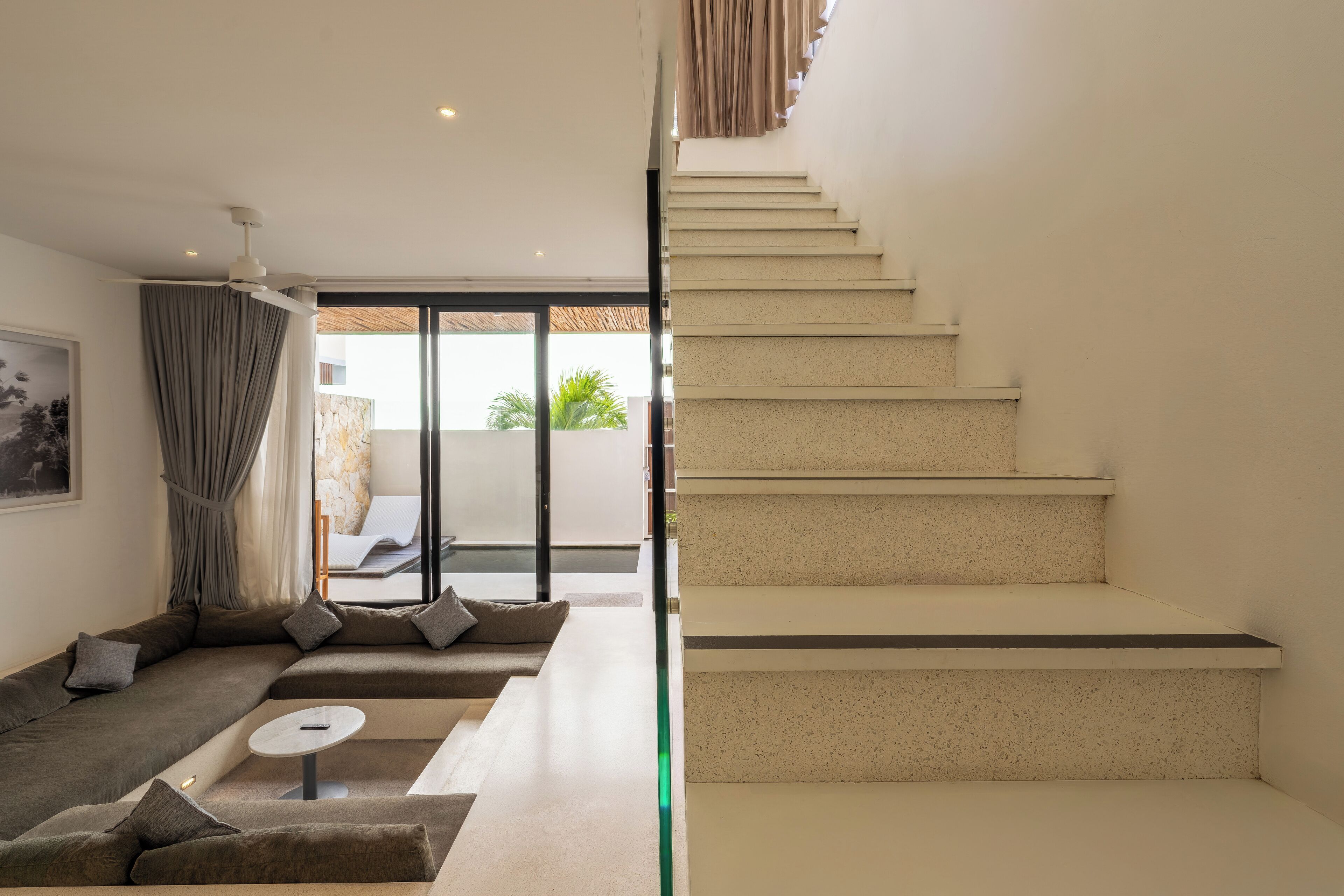 A modern living room with a sectional sofa, a coffee table, and a staircase leading to an outdoor area.