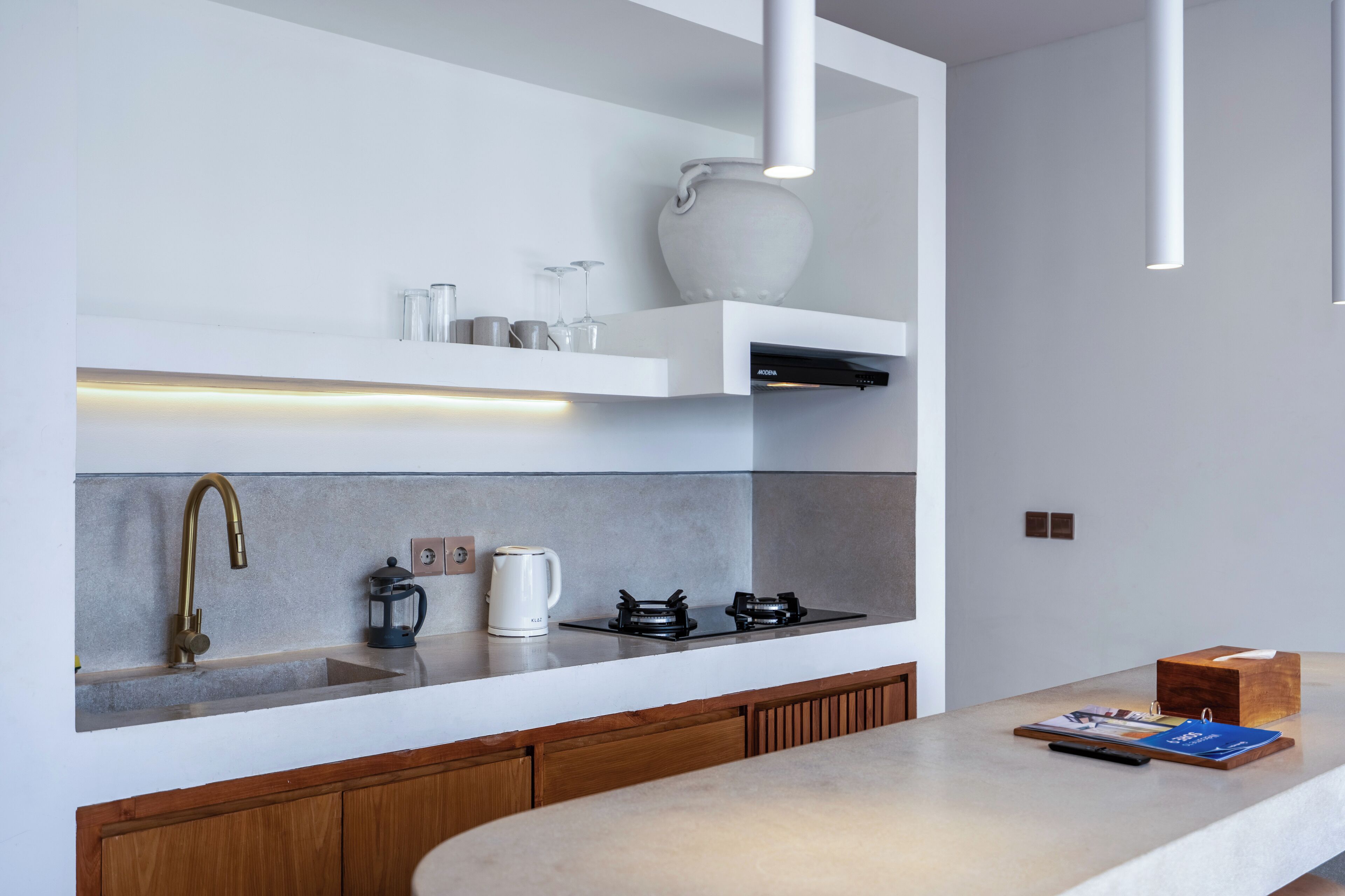 A modern kitchen with a built-in stove, a coffee maker, and a white vase on a shelf.