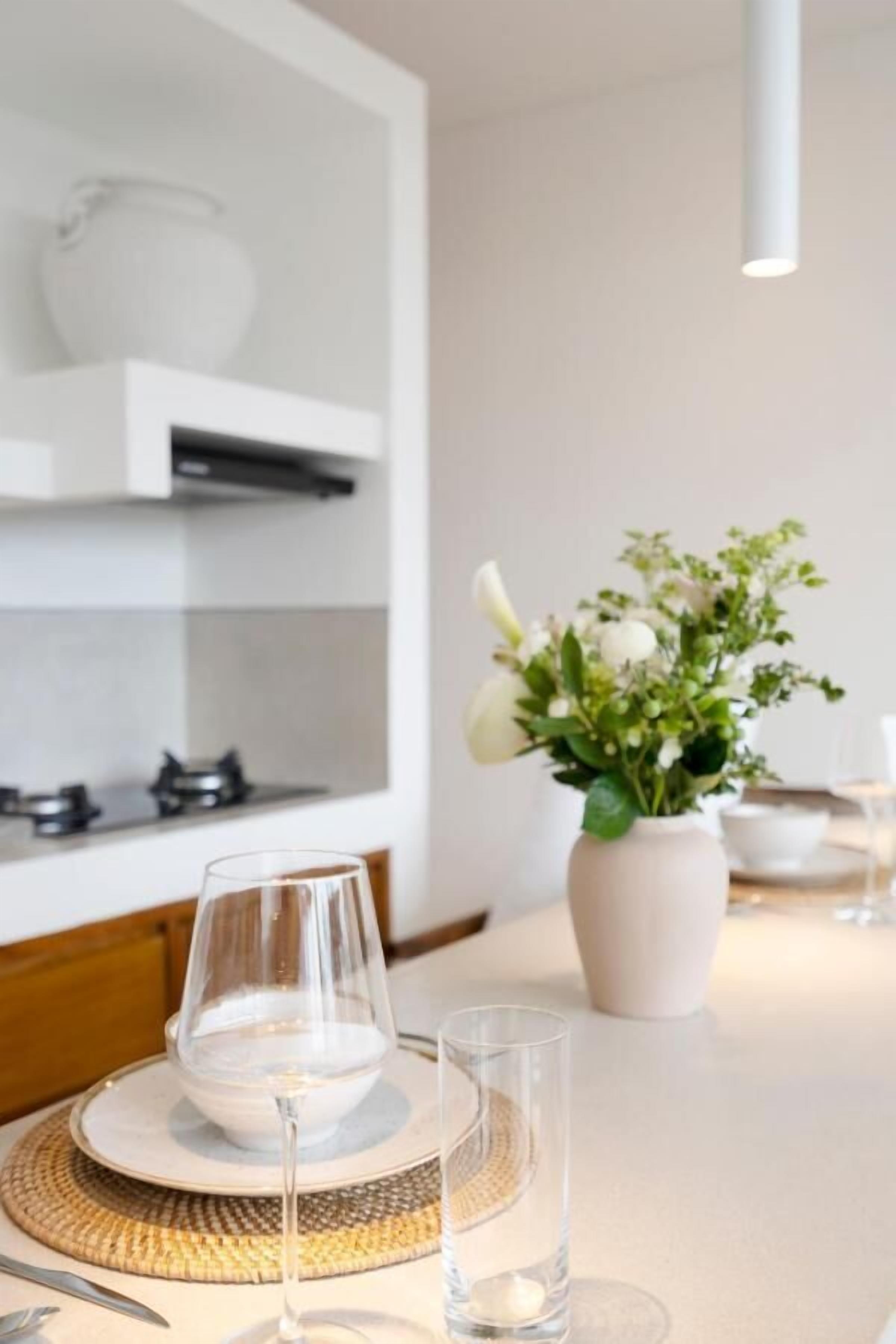 Et moderne spiseområde med et hvidt bord dækket til to, en vase med hvide blomster og en hængende lampe.