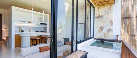 A modern interior with a kitchen area, a seating area with a bench, and a view of a stone wall and water feature.