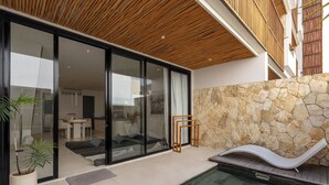 A modern outdoor pool area with a stone wall, a lounge chair, and a glass door leading to a living area. - Sore Pererenan Luxury Suites by Betterplace (Pererenan)