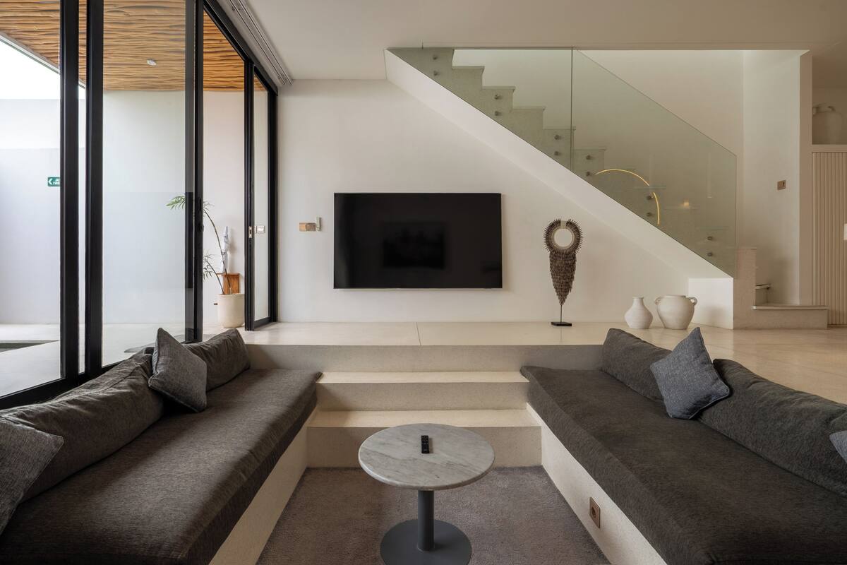 Un salon moderne avec un canapé, une table basse ronde et un escalier doté de rampes en verre.