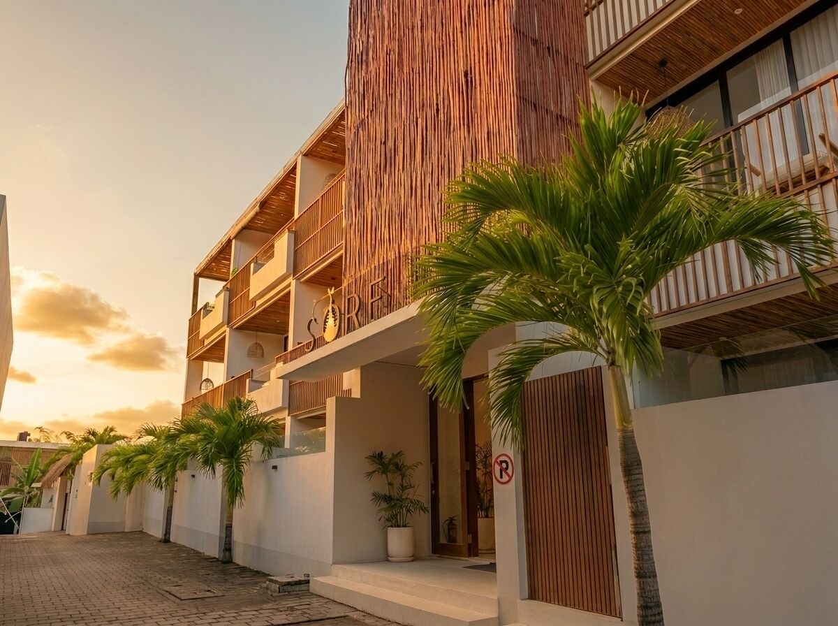A multi-story building with balconies, a gated entrance, and palm trees.