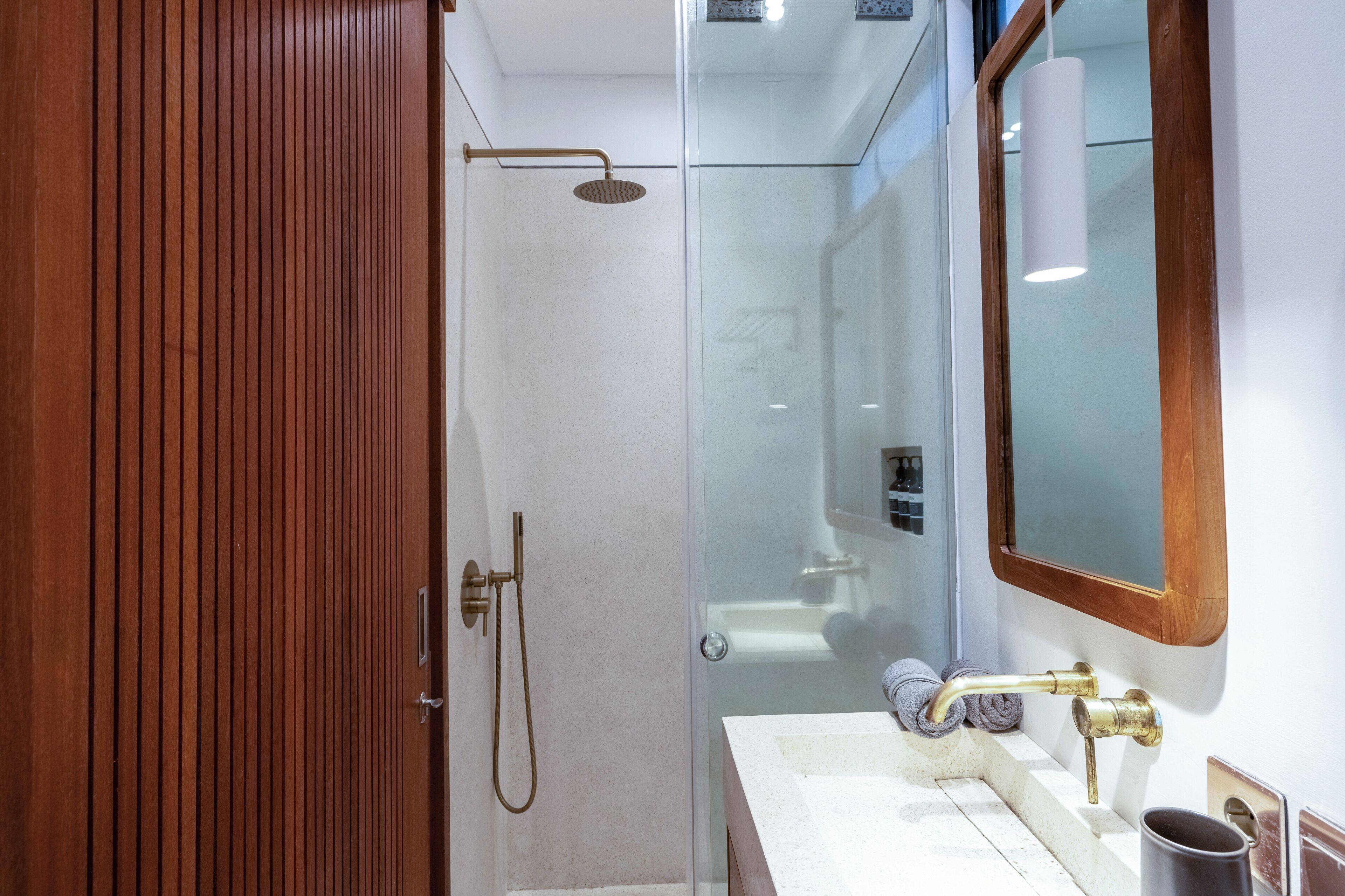 A modern bathroom with a wooden door, a glass shower enclosure, and a sink with a mirror.