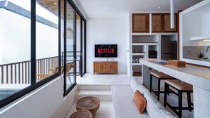 A modern kitchen with a flat-screen TV displaying 'NETFLIX', wooden cabinets, and a bar area with stools. - Sore Pererenan Luxury Suites by Betterplace (Pererenan)