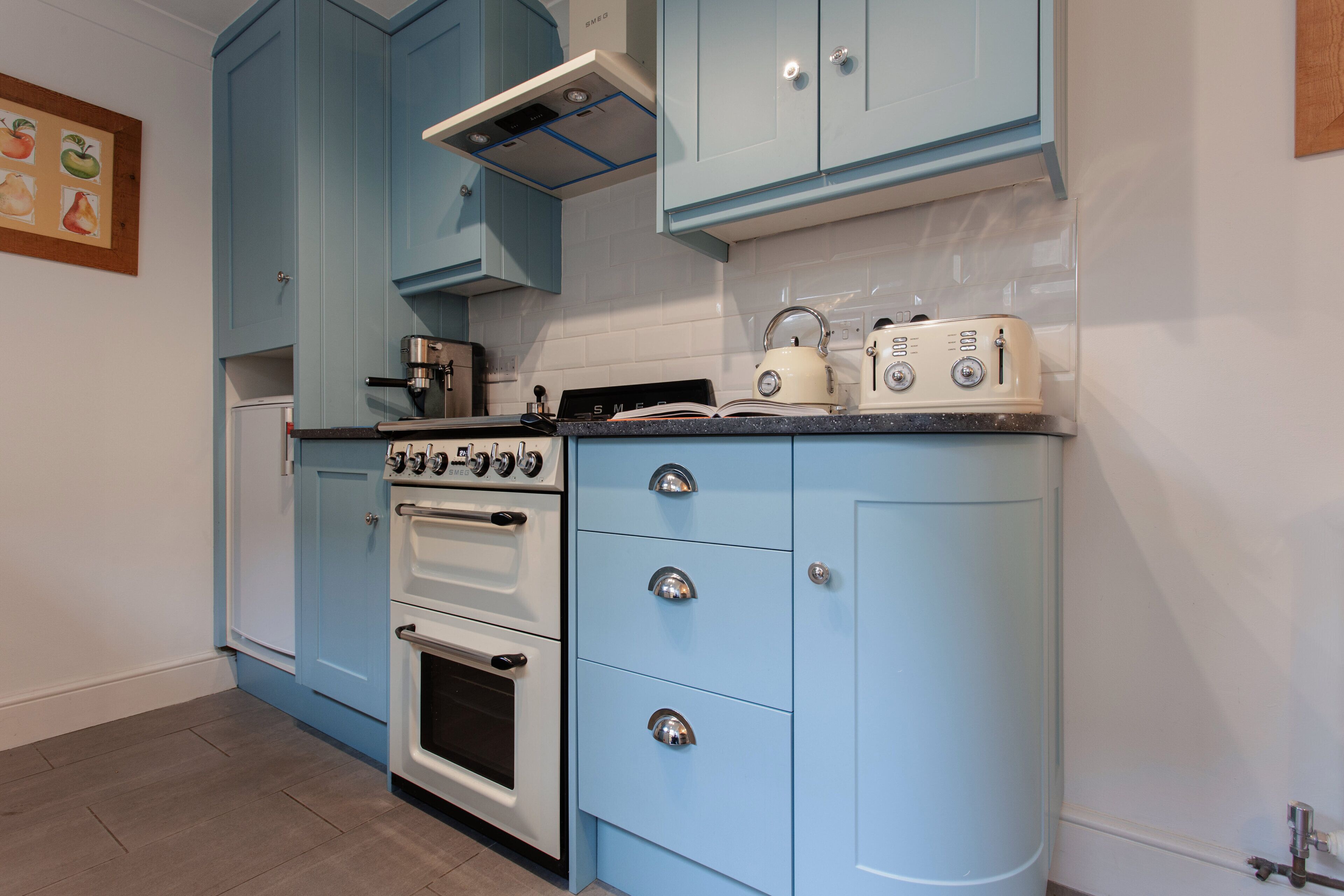 A compact kitchen with blue cabinets, a white stove, and a countertop with a kettle and toaster.
