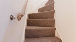 Un escalier avec des marches recouvertes de moquette et une porte dotée d’une poignée en corde.
