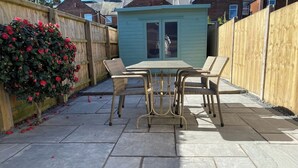 Une terrasse avec un sol en pierre, une table et quatre chaises en osier.