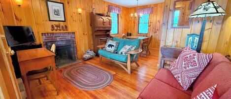A cozy cabin interior with a fireplace, wooden walls, a sofa, and a dining area.