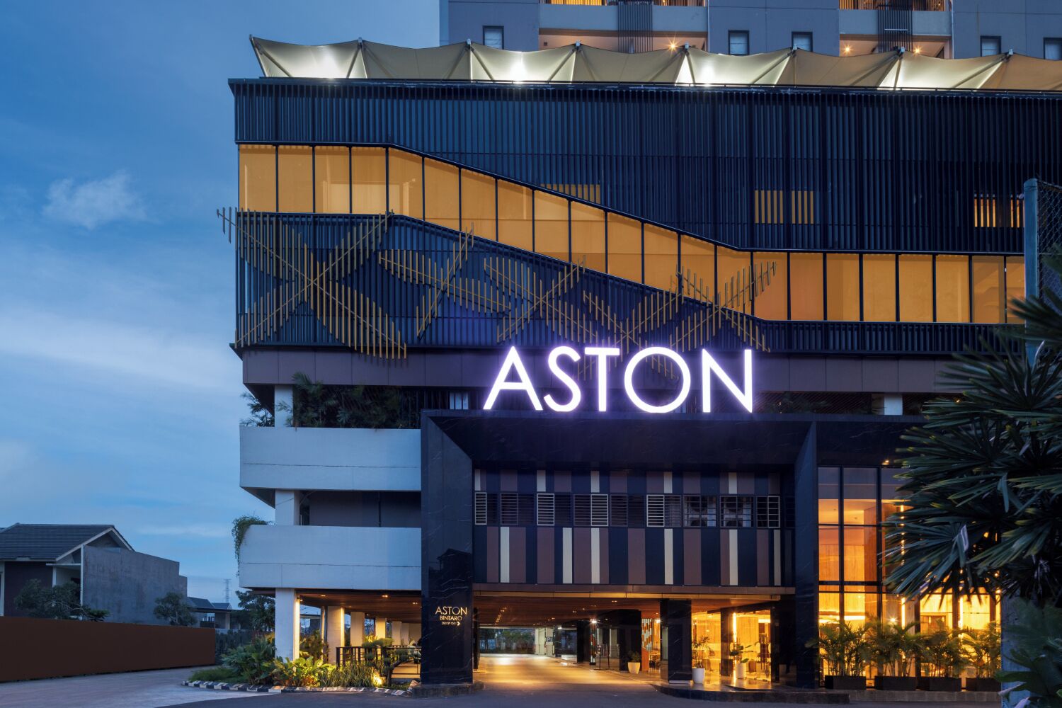 Un hotel moderno con un llamativo letrero 'ASTON', que presenta un diseño contemporáneo con una mezcla de elementos de vidrio y metal.
