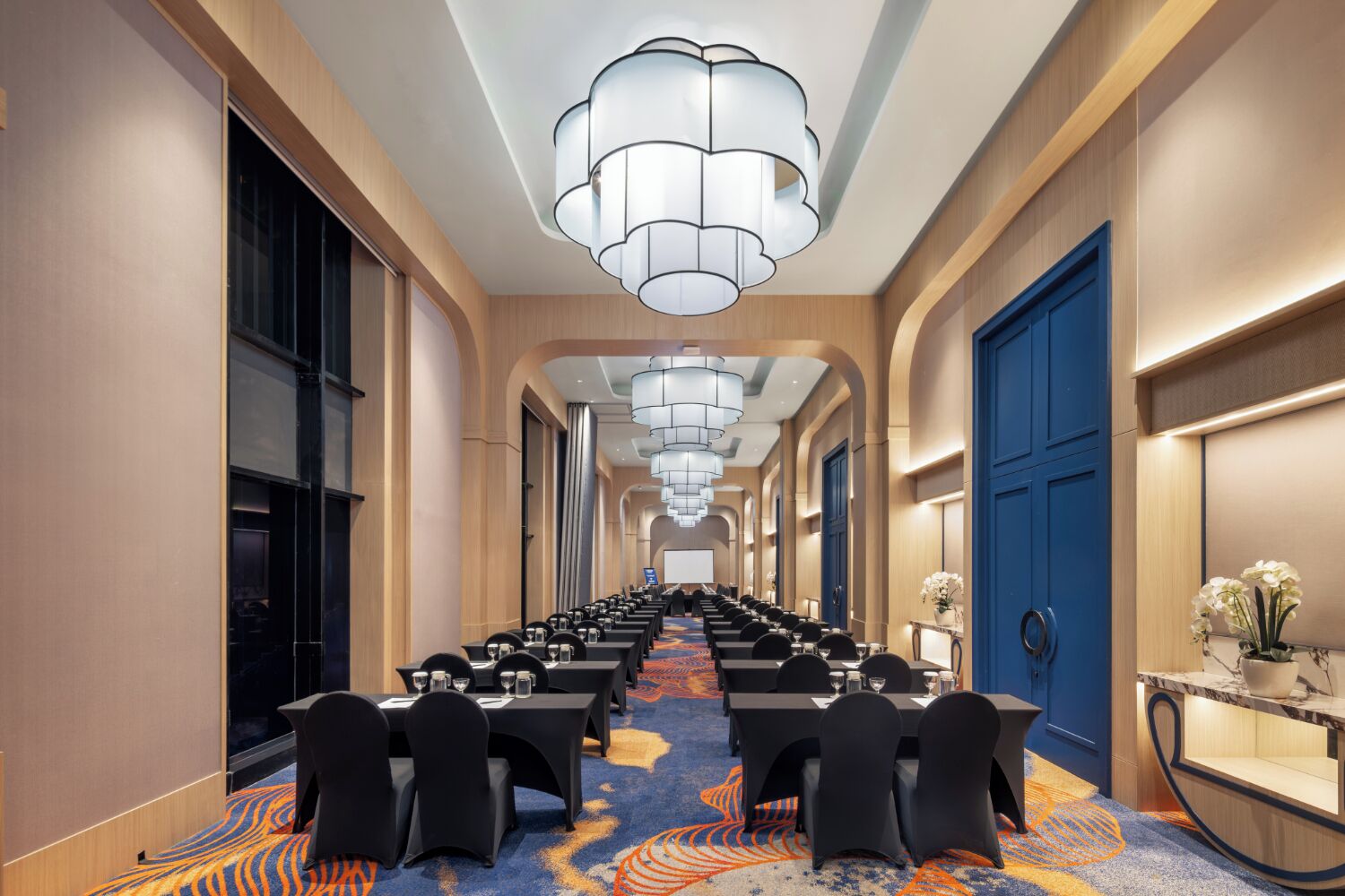 A long conference room with tables and chairs, a chandelier, and a blue door.