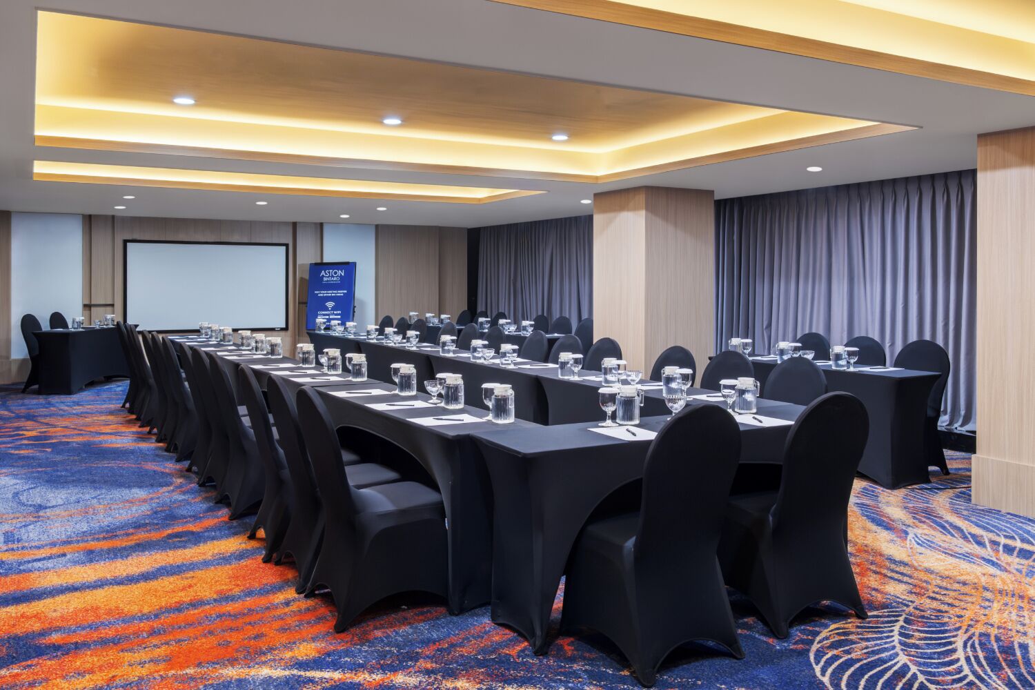 A conference room with long tables, chairs, and a projector screen.