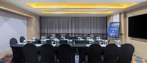 Une salle de conférence avec une longue table, des chaises noires et un panneau bleu.