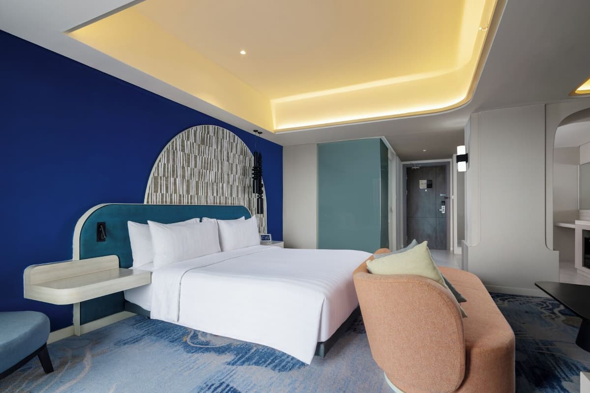 A modern hotel room with a large bed, a seating area, and a unique ceiling design.