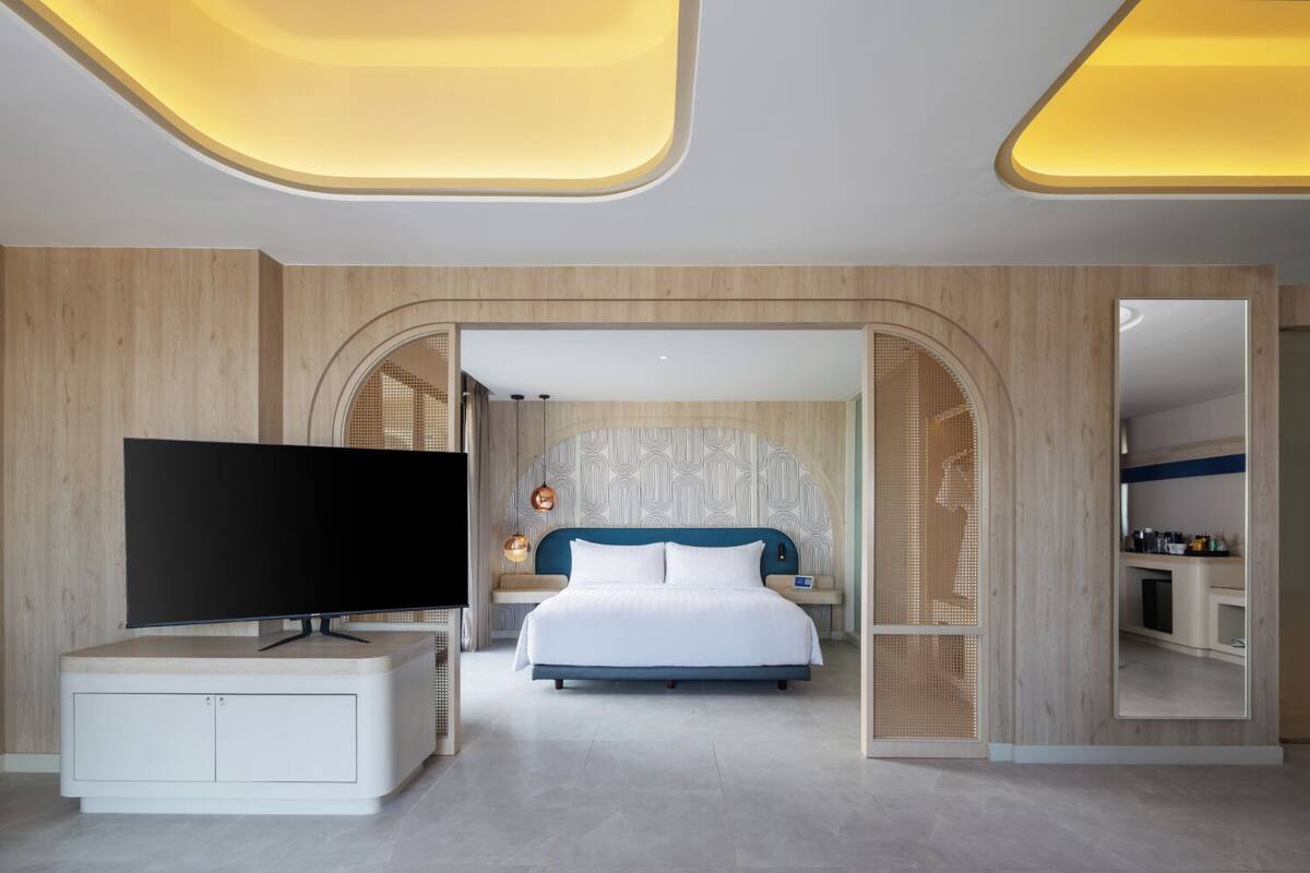A modern hotel room with a large bed, a TV, and a wooden wardrobe.