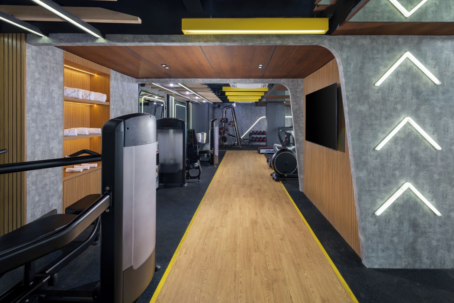 Un gimnasio con equipamiento de ejercicio, piso de madera y una pista de atletismo amarilla.