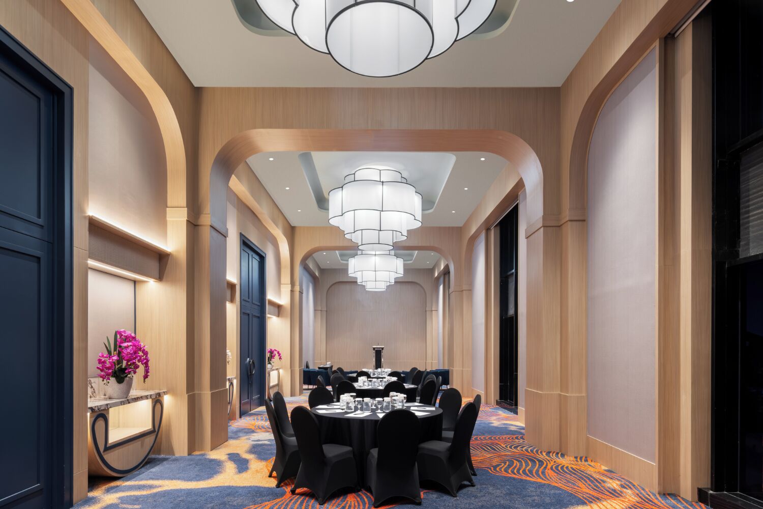 Un pasillo de hotel con una mesa redonda dispuesta para comer, flanqueado por paneles de madera y una alfombra estampada.
