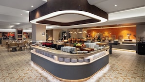 Un moderno vestíbulo de hotel con una zona de buffet central, arreglos de asientos y una pared decorativa.