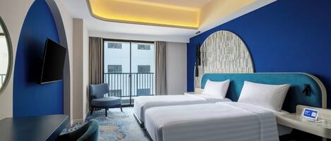 A hotel room with two beds, a desk, a chair, a TV, and a balcony with a city view.