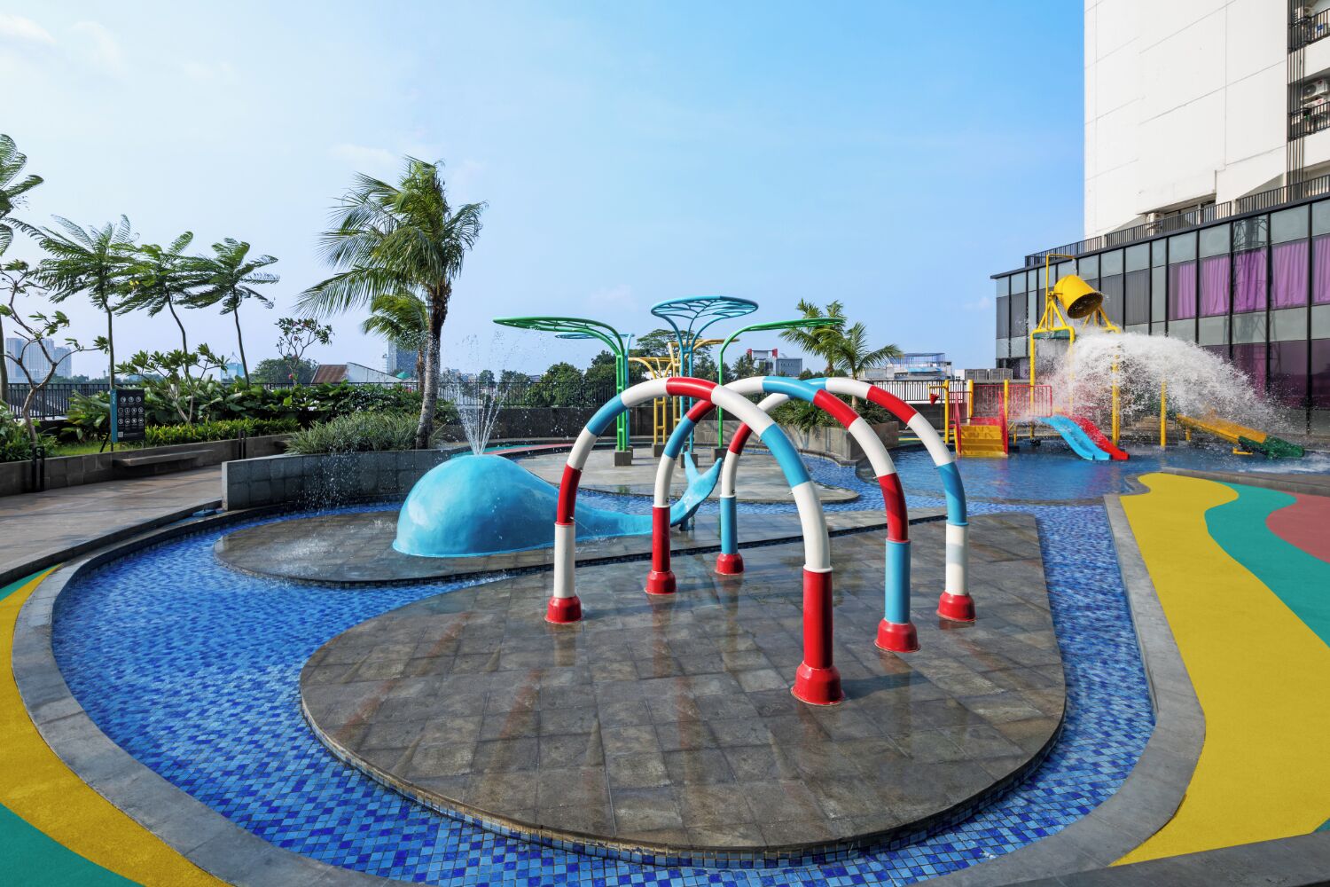 Een waterpark met verschillende glijbanen en fonteinen, omringd door een betegeld zwembad en palmbomen.