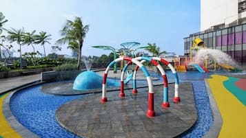 Een waterpark met verschillende glijbanen en fonteinen, omringd door een betegeld zwembad en palmbomen.