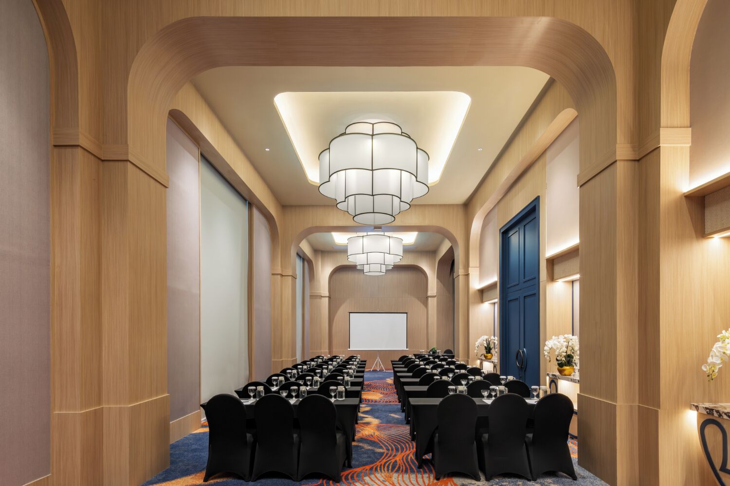 A conference room with long tables, black chairs, and a chandelier.