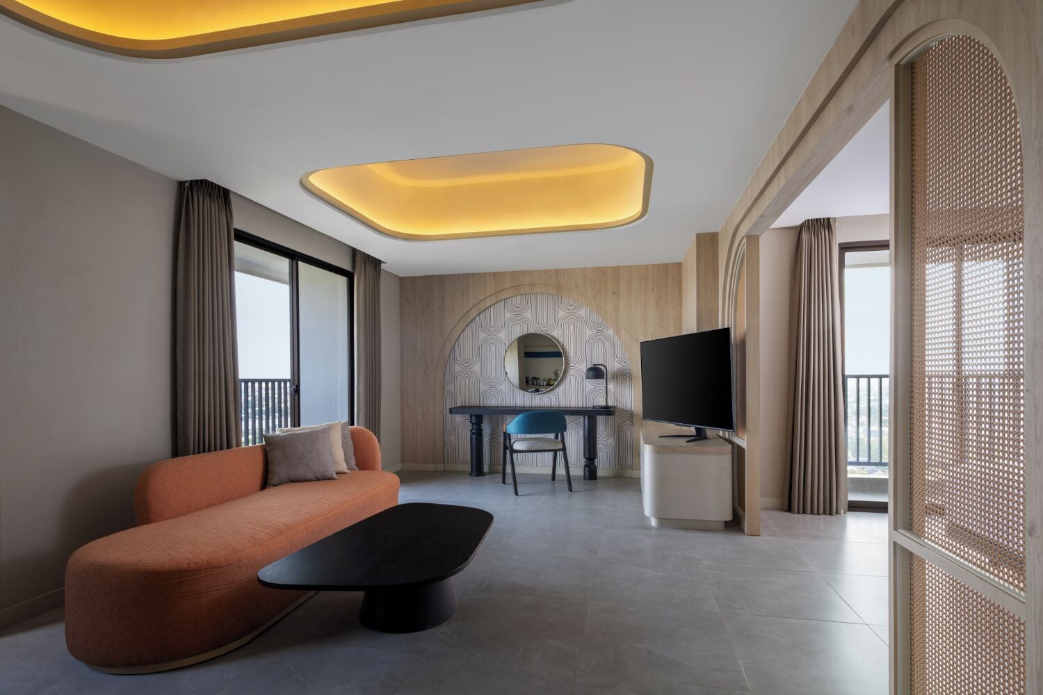 A modern hotel room with a sofa, a dining table with chairs, a TV, and a balcony with a view.