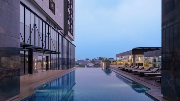 Una piscina infinita en la azotea con sillones reclinables, arquitectura moderna y una vista despejada del paisaje urbano.