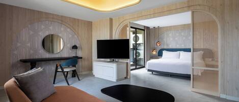 A modern hotel room with a sofa, a desk with a TV, a bed, and a balcony with a view.