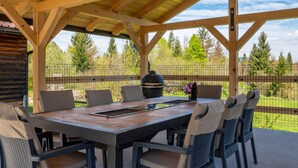 A covered outdoor dining area with a wooden table and chairs, surrounded by a wooden fence and trees. - Relax & Play by Interhome (Čabar)